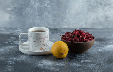 Cup of tea, lemon and bowl of dried flowers on marble background