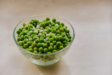 Frozen green peas in a glass plate stands on a wooden kitchen