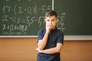 Cute boy stand in the classroom background of blackboard. Education. Elementary school. Boy thinking about math