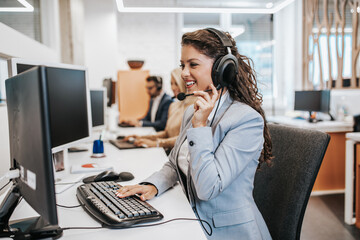 Beautiful smiling female call center worker accompanied by her team working in the office.