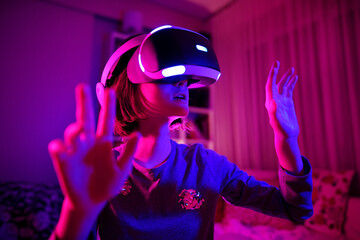 Pretty teenage girl wearing virtual reality headset in a dark room. Cute teen using VR glasses to play a game. Child in virtual augmented reality helmet.