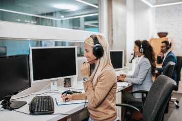 Beautiful blond smiling female call center worker accompanied by her team working in the office.