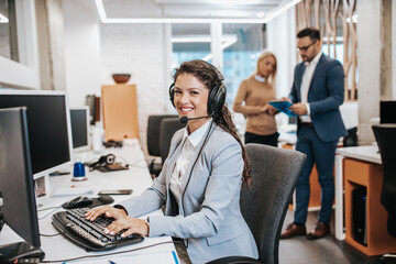 Beautiful smiling female call center worker accompanied by her team working in the office.