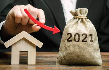 A businessman holds an arrow down near the house and a 2021 money bag. Forecasting the real estate...