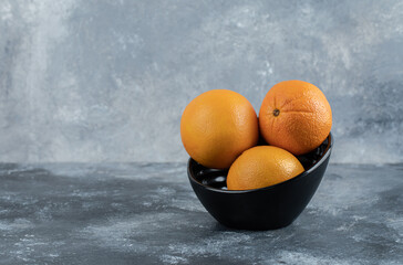 Three fresh oranges in black bowl