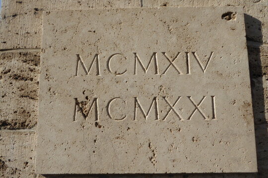 R&ouml;mische Zahlen MCMXIV und MCMXXI eingraviert in wei&szlig;en Stein. &Uuml;bersetzung: 1914 und 1921. Diese Steintafel h&auml;ngt in K&ouml;ln: Englischer Friedhof auf dem S&uuml;dfriedhof in K&ouml;ln.