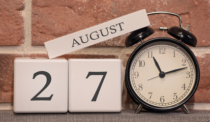 Important date, August 27, summer season. Calendar made of wood on a background of a brick wall. Retro alarm clock as a time management concept.