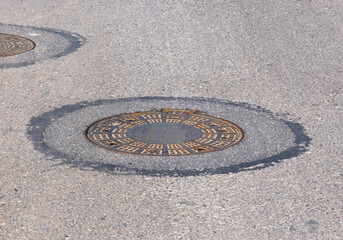 An old sewer manhole cover surrounded by an asphalt street