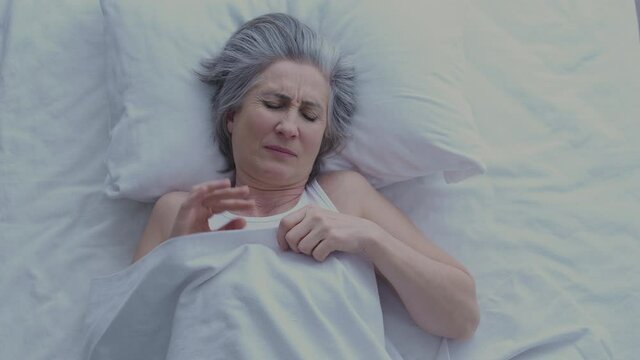 Unhappy tired mature woman awaking early in morning in bad mood, top view