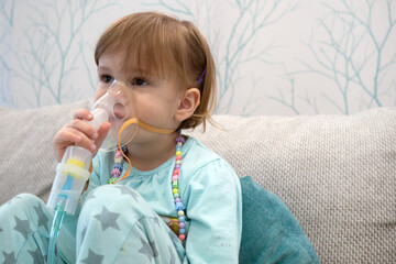 Kid girl makes inhalation with a nebulizer. sick child holding inhalator in hand and breathes...