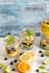 Summer healthy cocktails of citrus infused waters, lemonades or mojitos, with lime lemon orange blueberries and mint, diet detox beverages, in glasses on light background