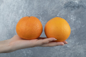 Male hand holding two oranges on marble background