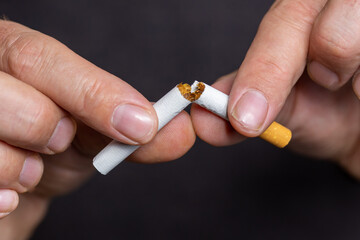 Person holds a cigarette with two hands and breaks it, symbolically for quitting smoking and paying attention to health