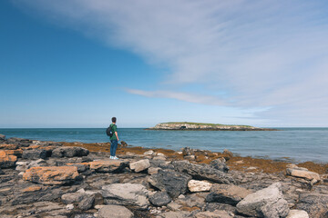 Fototapeta na wymiar Young man adventurer wearing a green t-shirt and a backpack looking to an island in the middle of the sea with a blue sky