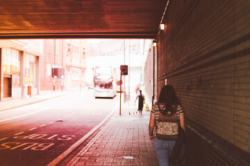 Young woman on her back wearing jeans with a backpack walking through a tunnel, next to a bus stop in Birmingham, United Kingdom