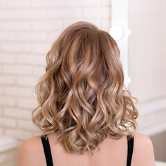 Female back with short, curly, natural blonde hair in hairdressing salon