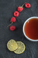 Fresh raspberries with tea and lemon on black background