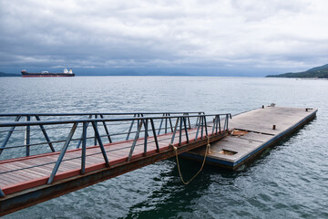 A walkway leading to a wooden platform on the sea in a cloudy day.