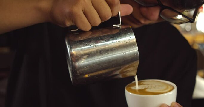 Barista making latte art in specialty coffee shop. Professional man making pouring stream milk with espresso