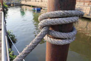 Fototapeta premium Marine ropes for towing ship bound around pipe steel post in the canal closeup.