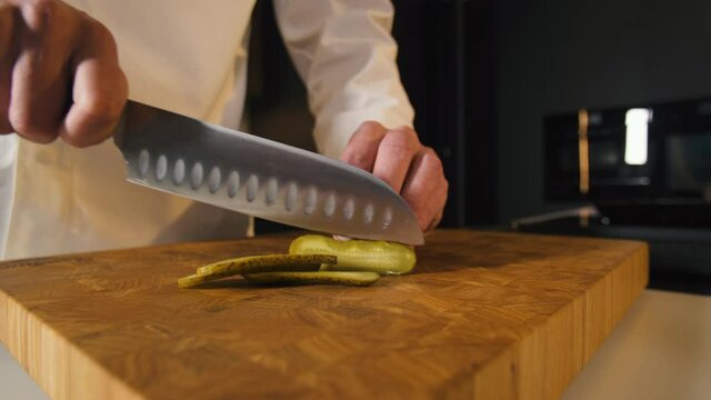 Chef Preparing Healthy Vegetarian Food in Modern Kitchen. Man Hands Cut Pickle Cucumber with Knife On Cutting Board. Vegetable Ingredients for Vegan Salad. Cooking Food In Restaurant Closeup