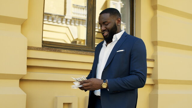 Smiling afro man counting money outside. Businessman walking with money outdoors - Powered by Adobe