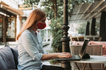 woman freelancer with face mask using laptop , online remote work outdoors