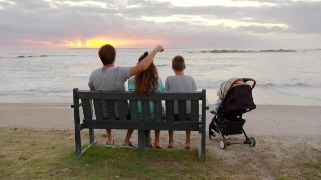 Happy family siting and looking out to the sunset together by the ocean.