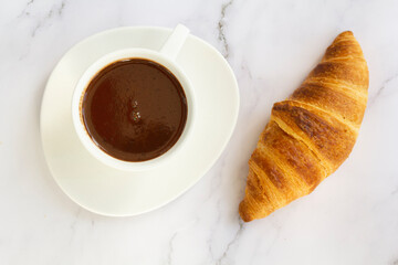 Top view of white cup with hot chocolate drink and french croissant