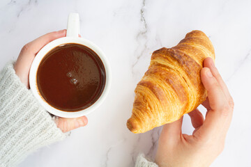 Top view of woman hand holding a cup with hot chocolate and a french croissant