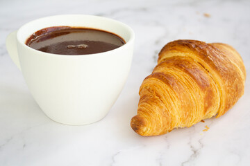 White cup with hot chocolate and french croissant on marble background
