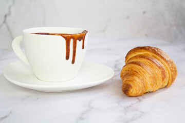 White cup with hot chocolate and french croissant on marble background