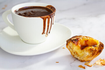 White cup with hot chocolate and portuguese custard tart called pastel de nata