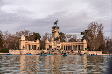 Fototapeta na wymiar Madrid, Spain; March 7, 2019. Monument to Alfonso XII in front of the lake in the Retiro Park. Tourists on the lake strolling with their boats.