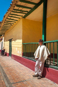 Vertical photo of a peasant wearing typical Boyaca dress next to an old colonial house in Sora, Boyacá, Colombia