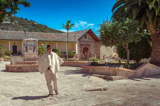 Peasant walks through the main park of Sora in Boyacá, Colombia with church in the background