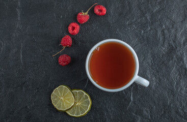 Obraz na płótnie Canvas Fresh raspberries with tea and lemon on black background