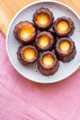 A close up of Canelés de Bordeaux on a white plate and pink table