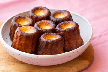 A close up of Canelés de Bordeaux on a white plate and pink table