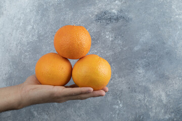 Male hand holding three oranges on marble background
