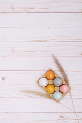 colorful eggs on white wooden background with the dry grass. Natural decor for Easter. 