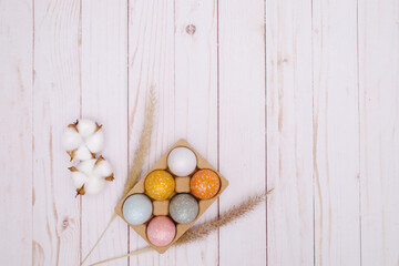 colorful eggs on white wooden background with the dry grass. Natural decor for Easter. 