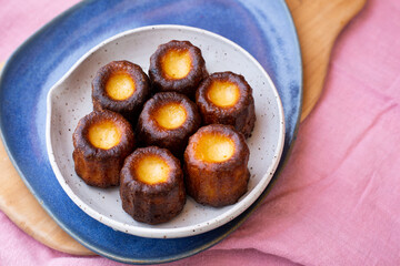 A small blue plate of Canelés de Bordeaux on a pink tablecloth