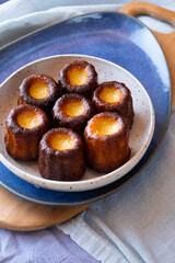 Canelés de Bordeaux on white and blue plates, wooden board and from the side