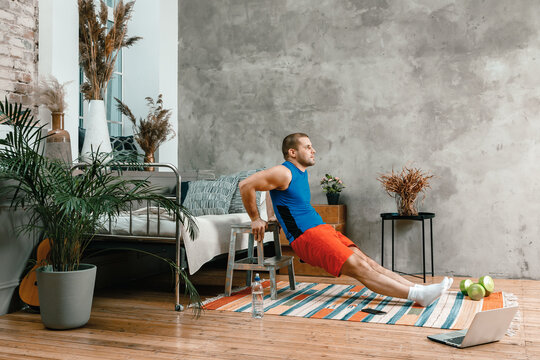 The Strong Man Goes In For Sports At Home. Cheerful Young Man With Black Hair Shakes Biceps, Do Push-ups On Stool   In The Bedroom