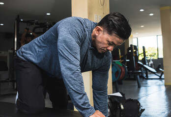 A buff asian man prepares to do dumbbell rows or tricep kickbacks. Focused and determined mindset at the gym.