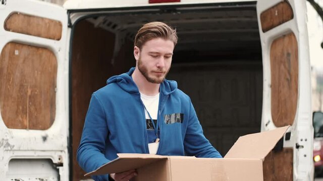 Delivery service. The man is checking what's inside paper box. Van at the background.