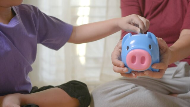 Happy Asian kid boy preschool and mother putting pin money coins into piglet. Little child putting coin into piggy bank for saving with pile of coins at home, Investment education concept, - Powered by Adobe
