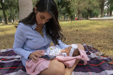 mama con bebe sentada en parque al aire libre usando teléfono móvil