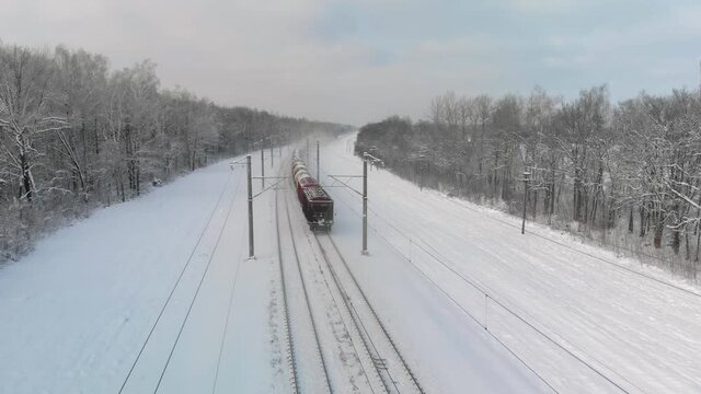 Freight train is moving through a rural wooded area on a frosty day in winter. Concept of trade and transportation. Top view from the back